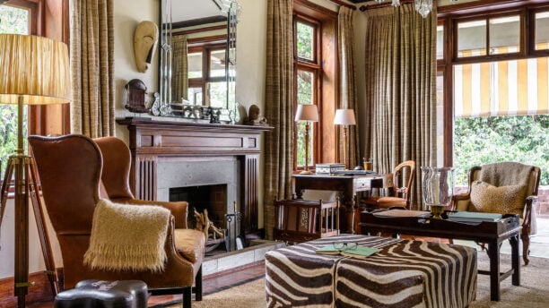 Interior of Singita Sasakwa living area, armchairs and coffee table facing open fireplace, Singita Grumeti Tanzania