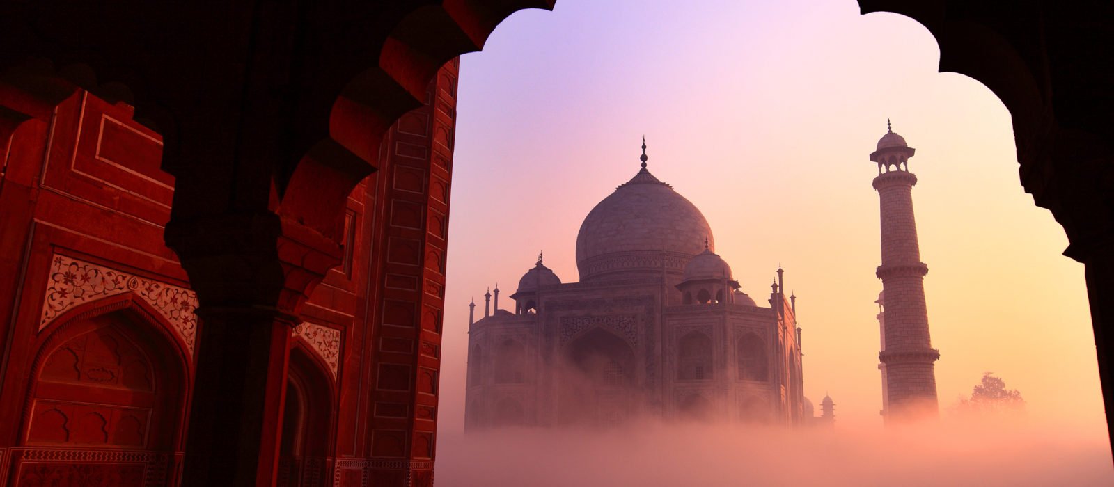 Taj Mahal in the warm pink and yellows of sunrise on a foggy morning