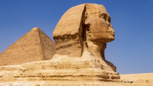 Sphinx carving in front of Egyptian pyramid with tourists below